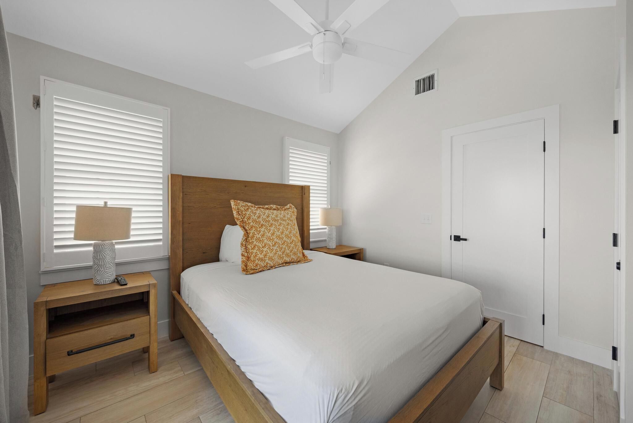 A bedroom with a bed, wooden headboard, bedside tables with lamps, a ceiling fan, and a white door.
