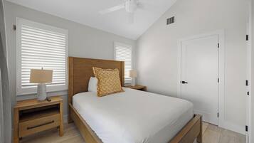 A bedroom with a bed, wooden headboard, bedside tables with lamps, a ceiling fan, and a white door.