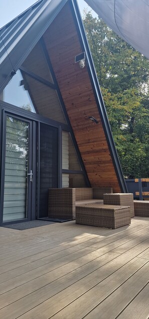 A modern house with a sloped roof, a wooden deck, and wicker furniture.