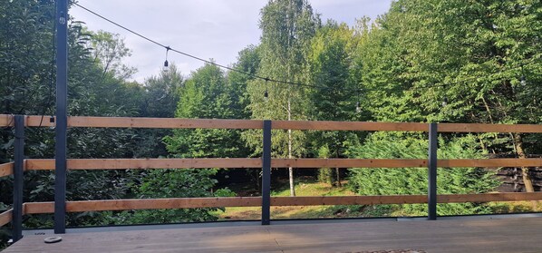 A wooden deck with a metal railing, surrounded by dense green foliage and trees.