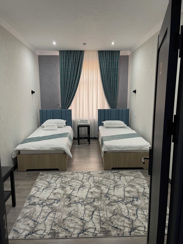 A hotel room with two single beds, a marble-patterned rug, and a window with curtains. - Mehran (Andijan)
