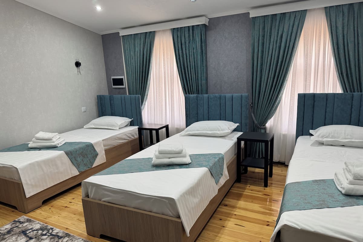 Habitación de hotel con tres camas individuales, una mesita y un televisor.