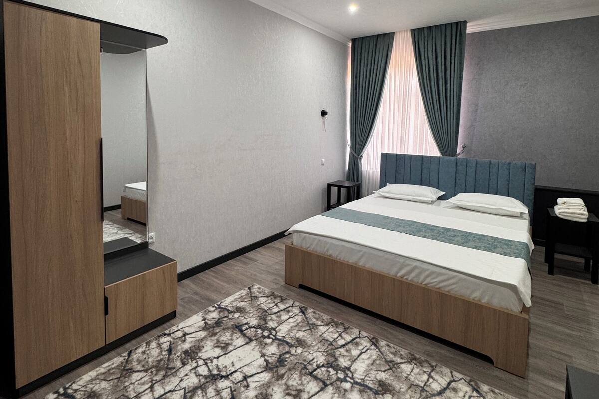 Una habitación de hotel moderna con una cama grande, un armario, un espejo, una mesita de noche y un escritorio.