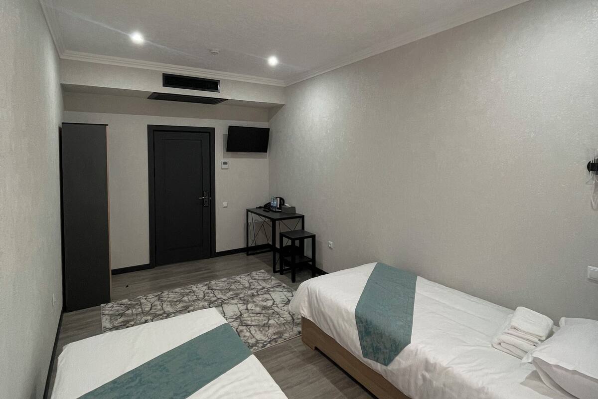 Habitación de hotel con dos camas individuales, un escritorio con silla, una mesita y un televisor en la pared.