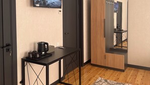 Una habitación de hotel moderna con suelo de madera, un escritorio negro con hervidor, televisión en la pared y un armario con espejo.