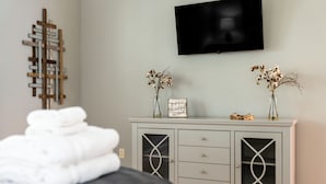 A bedroom with a bed, a grey cabinet with drawers, a television on the wall, and two vases with dried flowers. - Grove Hill - Spacious Home w/Hot Tub, 4 BRs, 4BAs, near downtown Dahlonega! (Dahlonega)