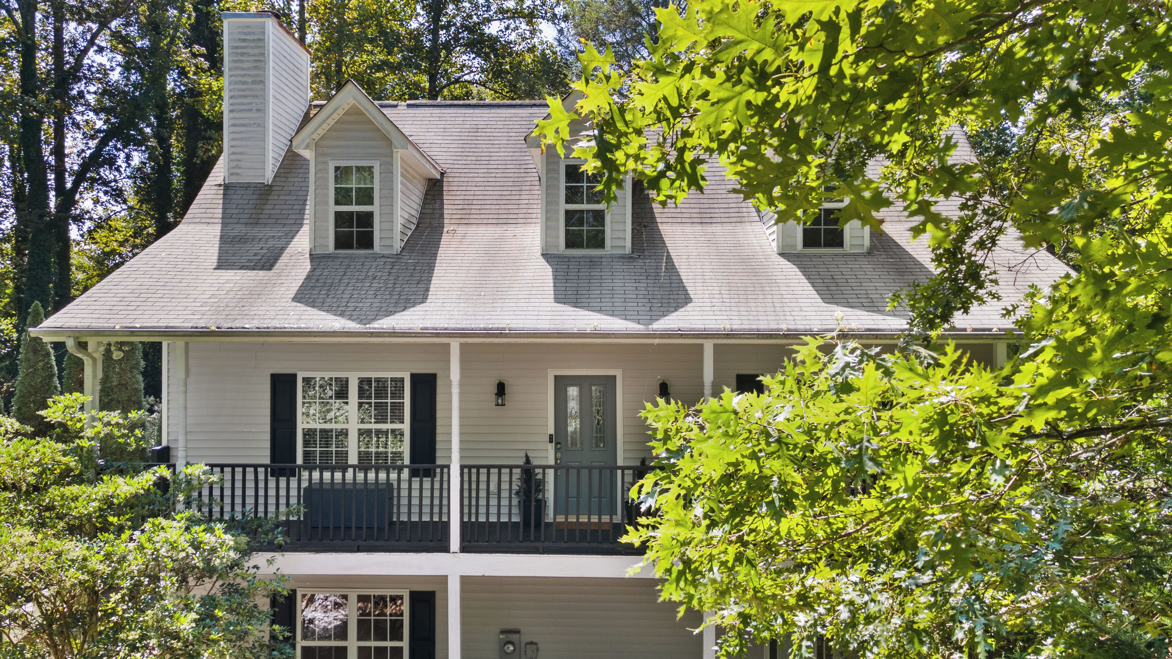 A two-story house with a gabled roof, dormer windows, and a front porch with a railing.