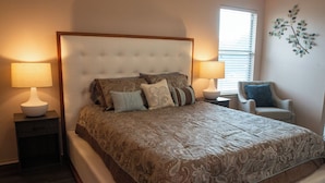 A bedroom with a large bed, two bedside tables with lamps, a chair, and a window with blinds. - Modern 3BR by Park, Sleeps 8, 1Gig Wi-Fi, Garage Parking (Pflugerville)