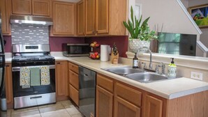 A modern kitchen with wooden cabinets, stainless steel appliances, a sink, and a potted plant. - Modern 3BR by Park, Sleeps 8, 1Gig Wi-Fi, Garage Parking (Pflugerville)