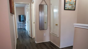 A hallway with a wooden floor, a mirror on the wall, and a door with a white frame. - Modern 3BR by Park, Sleeps 8, 1Gig Wi-Fi, Garage Parking (Pflugerville)