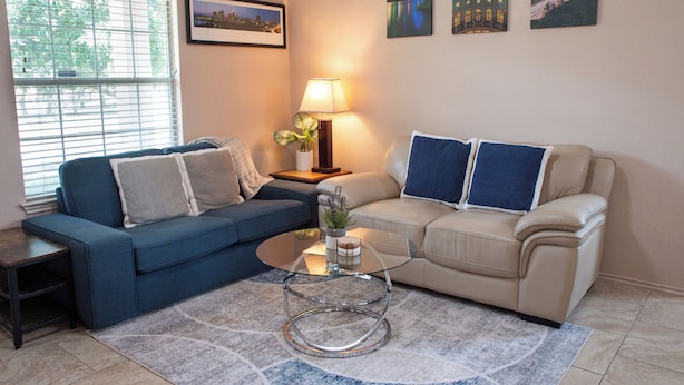 A living room with two sofas, a glass coffee table, a lamp, and framed pictures on the wall. - Modern 3BR by Park, Sleeps 8, 1Gig Wi-Fi, Garage Parking (Pflugerville)