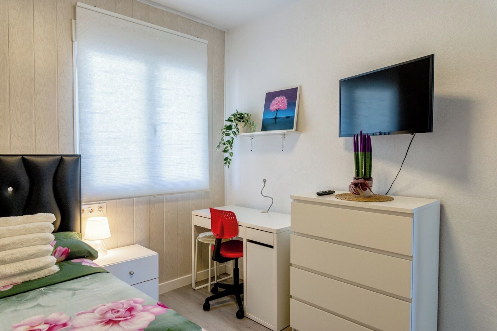 Un dormitorio con cama, escritorio, silla, televisor y cómoda.