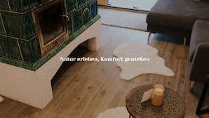 Una sala de estar acogedora con una chimenea de baldosas verdes, un alfombra mullida blanco y una mesa redonda de madera con una vela.