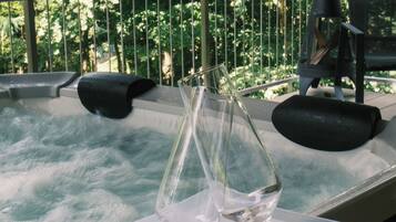 Een hottub met een glazen vaas en decoratieve objecten op een wit plateau, omringd door een metalen reling en weelderige beplanting op de achtergrond.