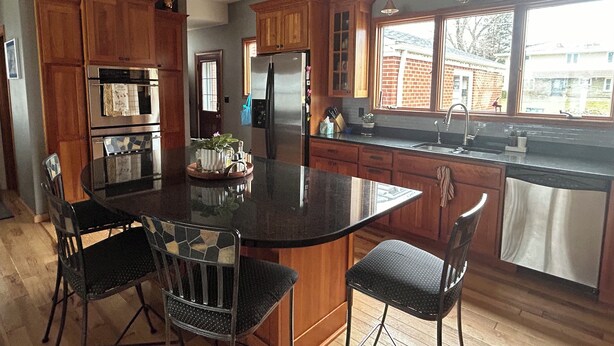 A modern kitchen with wooden cabinets, a stainless steel refrigerator, and a large island with chairs. - Luxury on the Lake (Storm Lake)