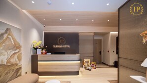 A reception desk with a logo, a sofa, a small table, and a decorative plant. - BLESSED Hotel Phu Quoc (Phu Quoc)