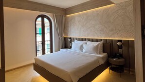 A modern hotel room with a large bed, a built-in headboard, and a view through a window with curtains. - BLESSED Hotel Phu Quoc (Phu Quoc)