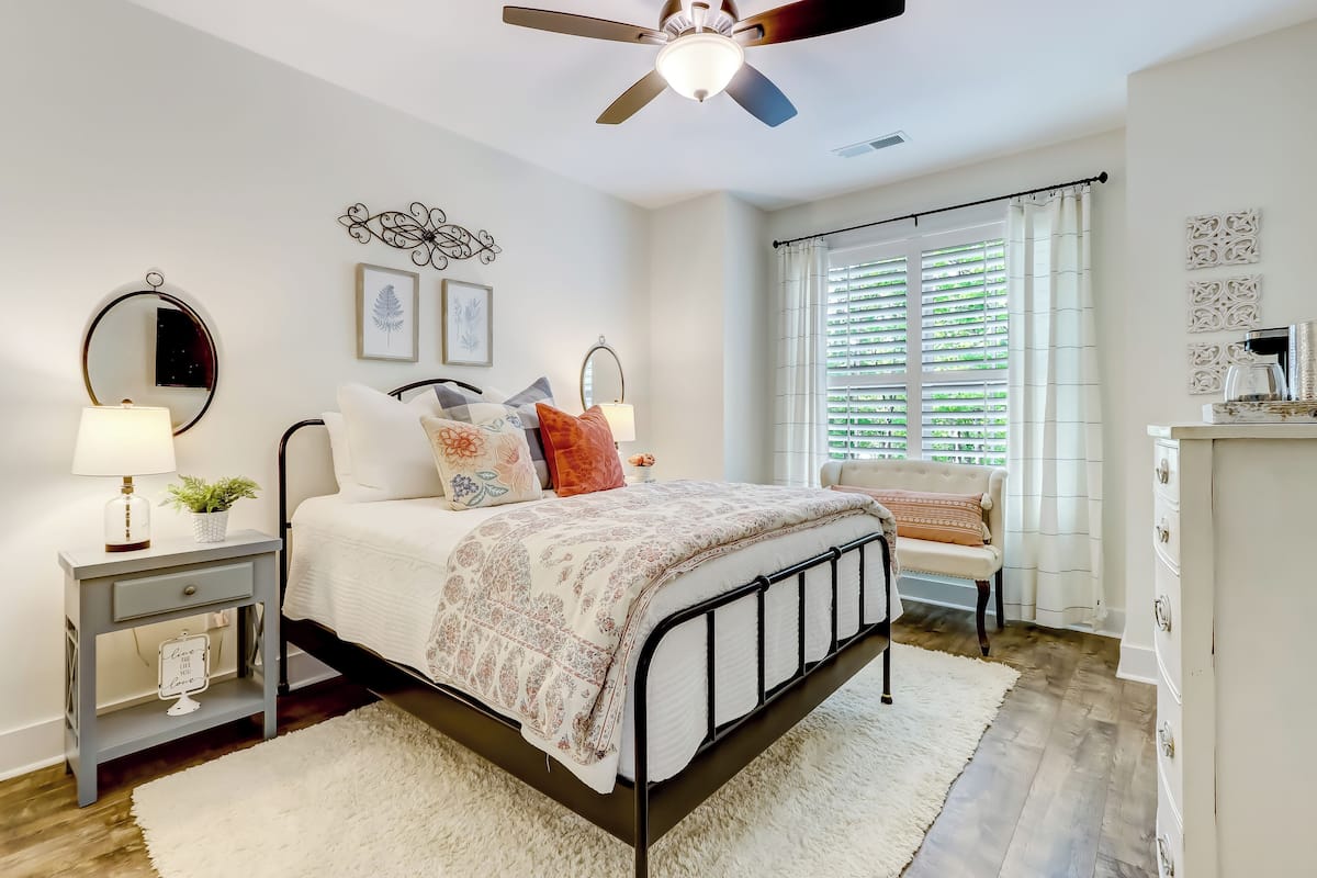 Quarto com cama, mesas de cabeceira, ventilador de teto, janela com persianas e cômoda.