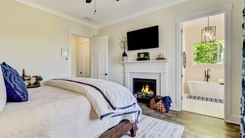 A bedroom with a bed, a fireplace, a television, and a bathroom visible through an open door.