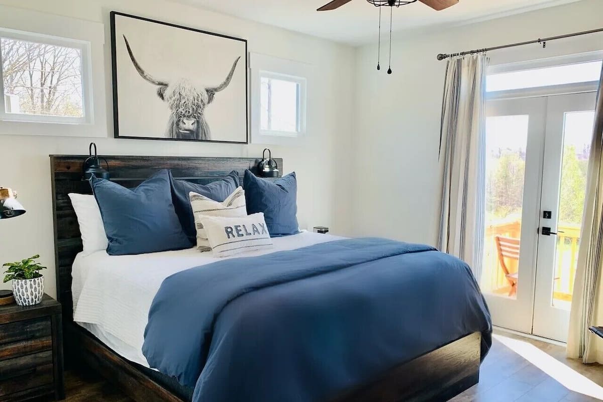 Quarto com cama, ventilador de teto, obra de arte emoldurada, mesa de cabeceira e vista para o exterior.