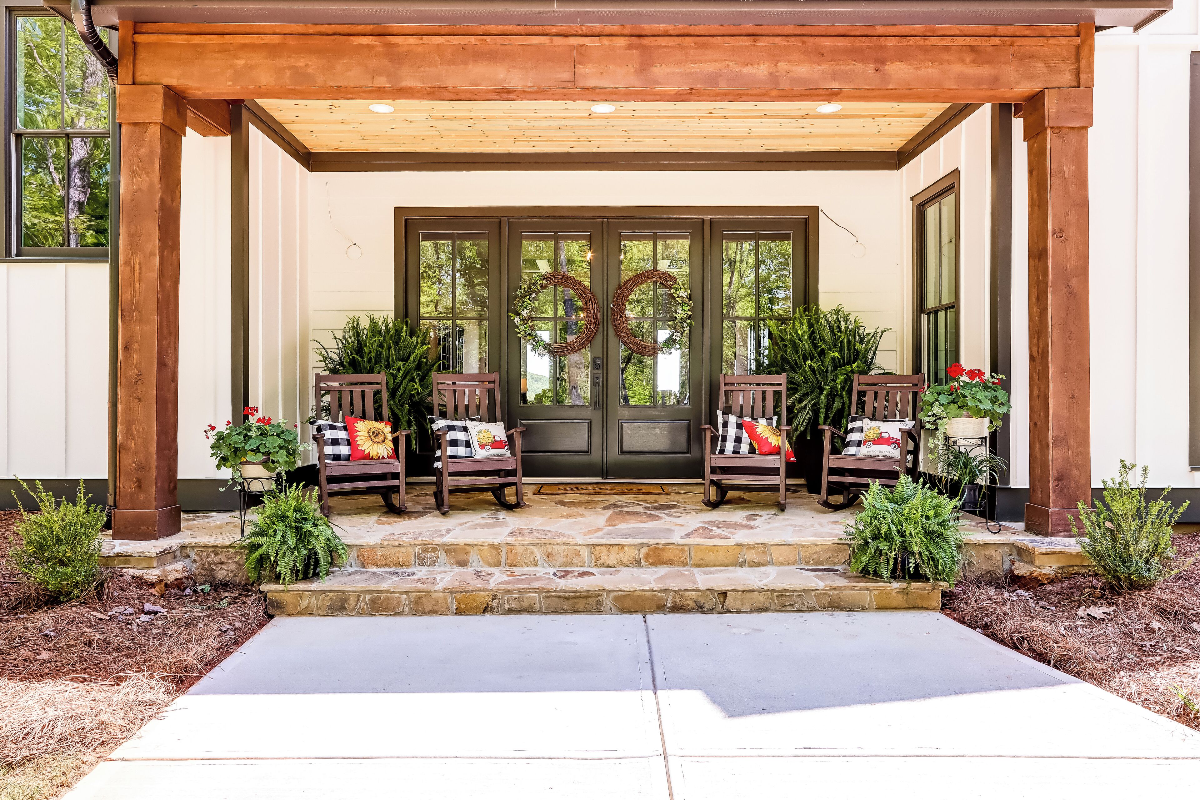 A covered porch with two rocking chairs, a stone entrance, and a door with a wreath.