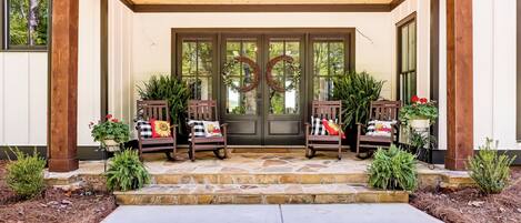 A covered porch with two rocking chairs, a stone entrance, and a door with a wreath.