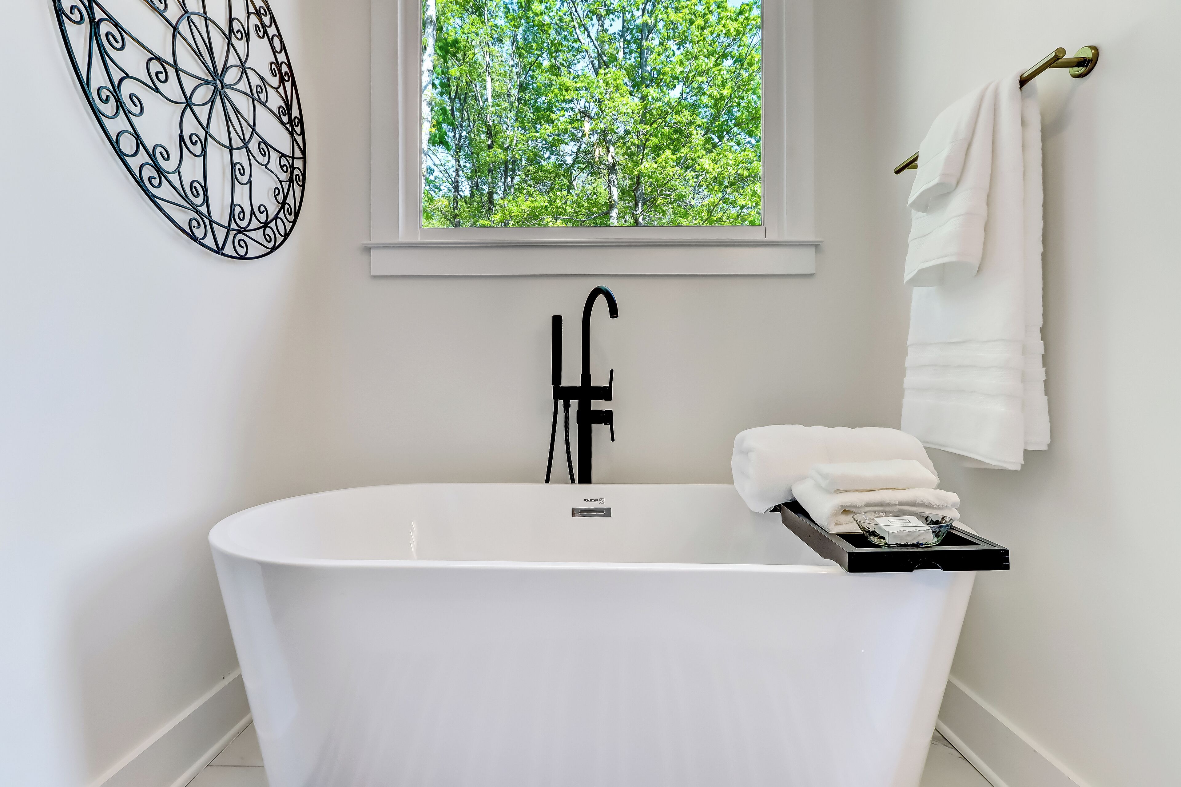 Un baño moderno con una bañera independiente, un ventanal con vistas a árboles y un perchero con toallas.
