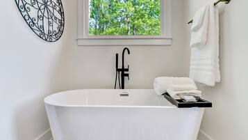 Un baño moderno con una bañera independiente, un ventanal con vistas a árboles y un perchero con toallas.