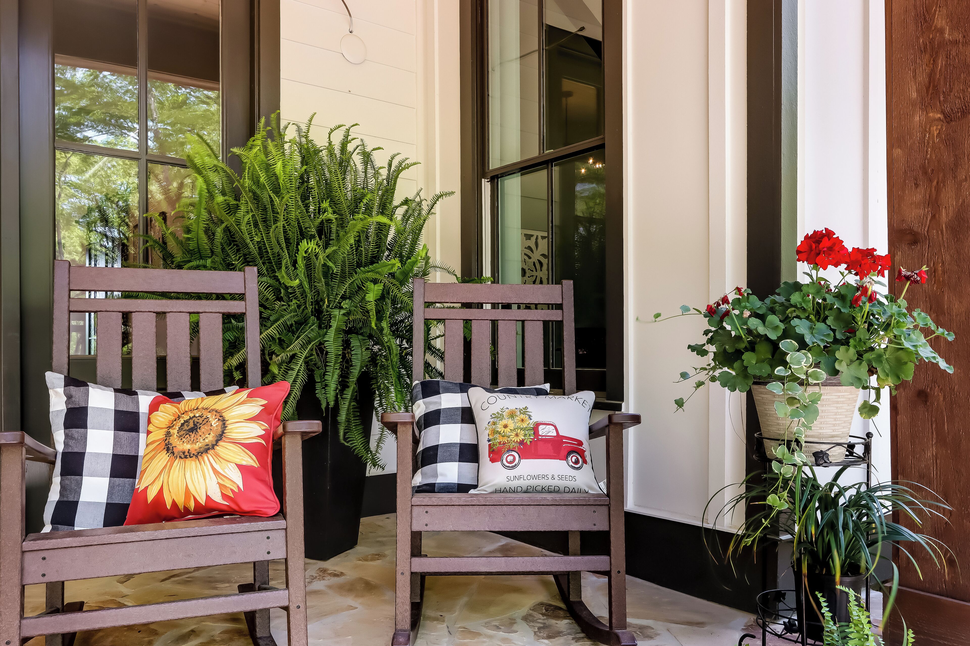 Deux chaises en bois avec des coussins à carreaux, une grande fougère en pot et une petite plante en pot aux fleurs rouges.