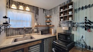 A kitchen with a sink, stove, and shelves with dishes.