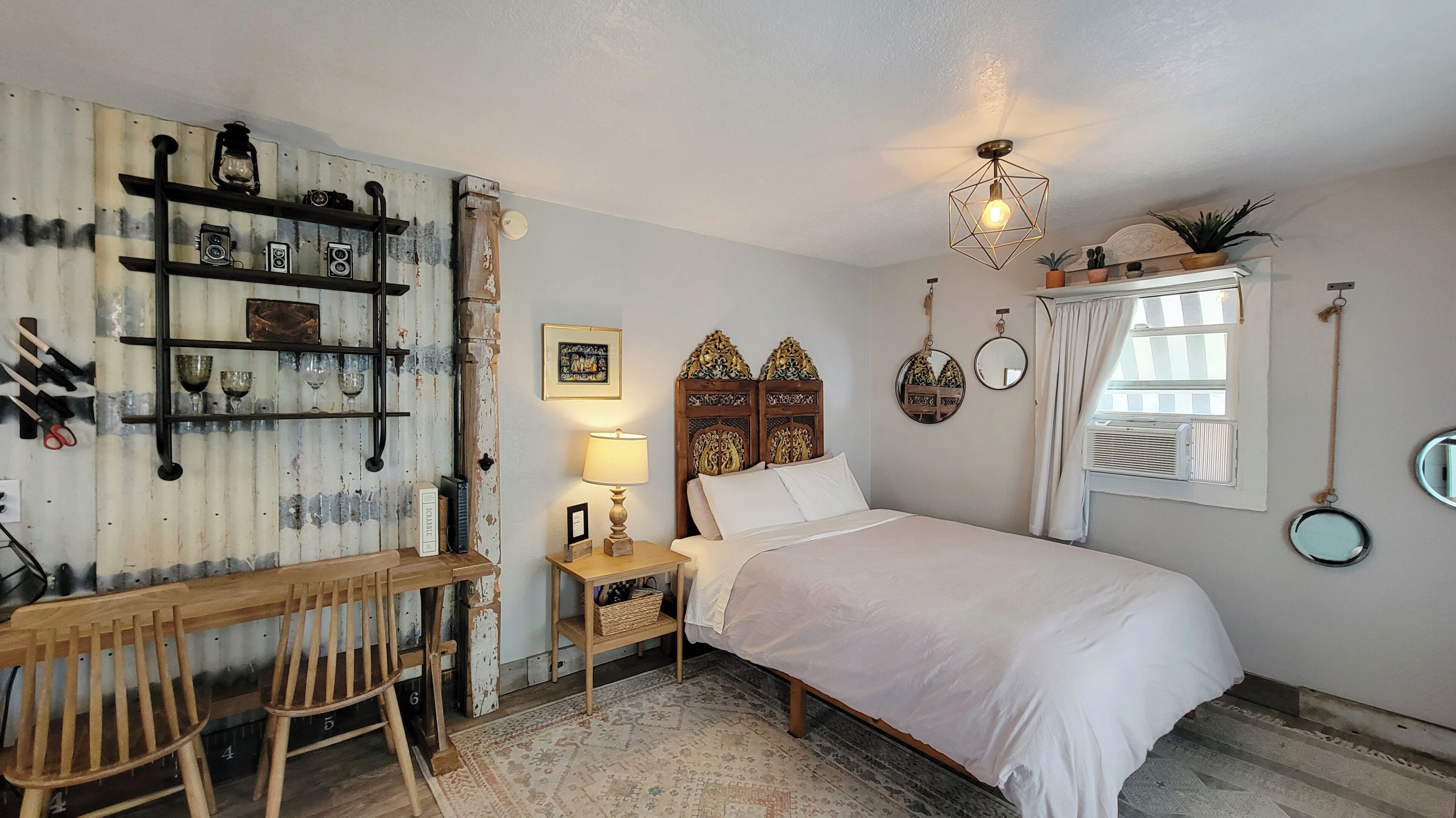 Ein Schlafzimmer mit einem hölzernen Bett, einem Schreibtisch mit Stühlen, einer Lampe und einer rustikalen Wand mit Regalen.