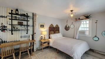 A bedroom with a wooden bed, a desk with chairs, a lamp, and a rustic wall with shelves.