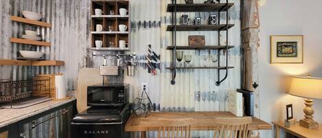 Una cocina con un horno Galanz, repisas de madera con vajilla, un microondas y una mesa de comedor con sillas.