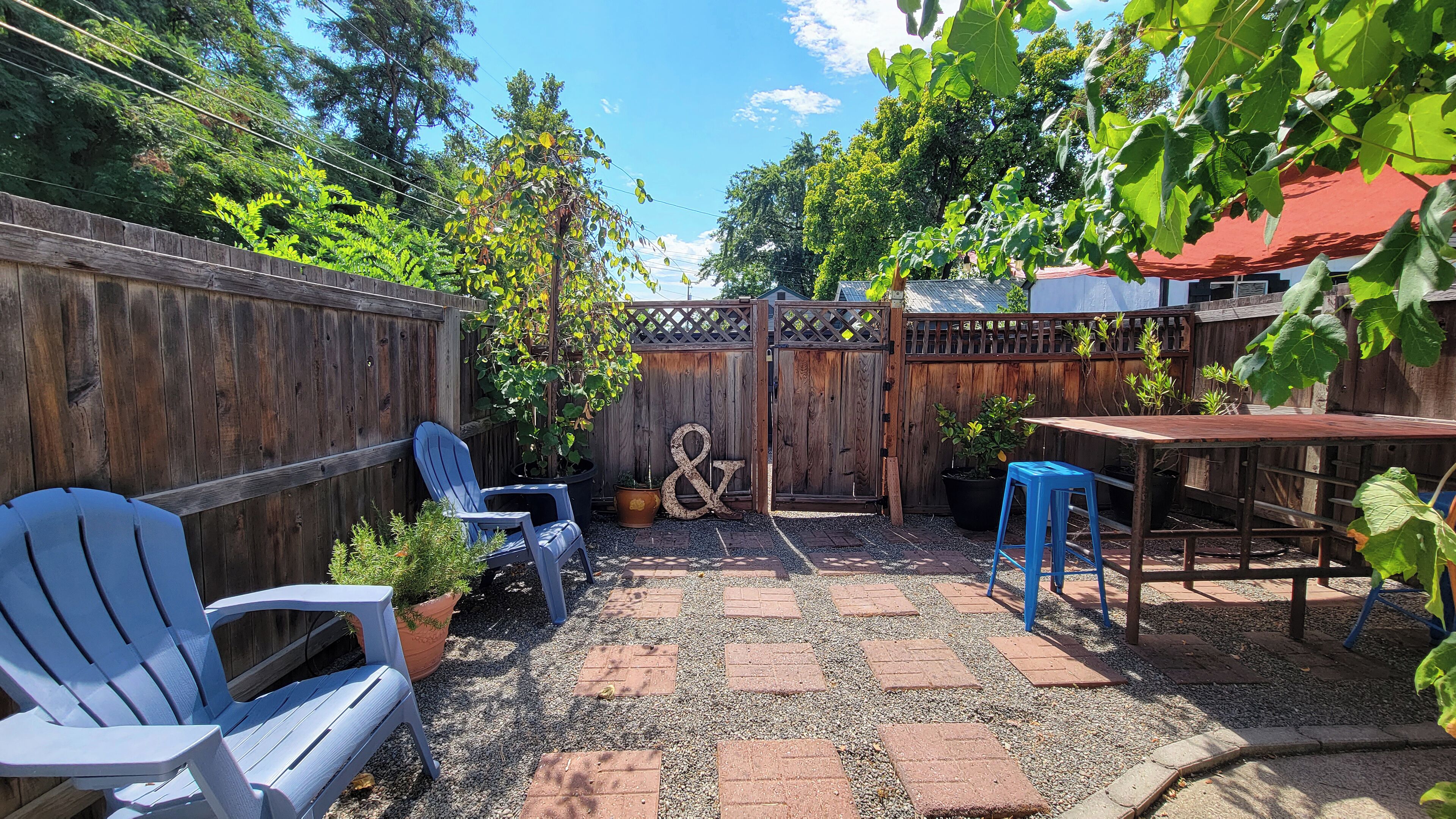 A backyard with a wooden fence, a patio table, blue chairs, and a small garden area.
