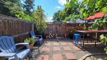 A backyard with a wooden fence, a patio table, blue chairs, and a small garden area.