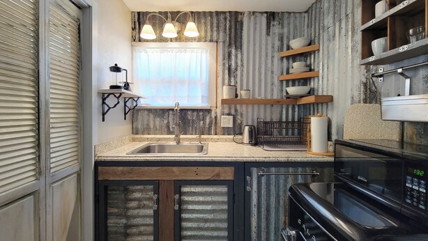A kitchen with a stainless steel sink, wooden cabinets, a black stove, and a window with curtains.