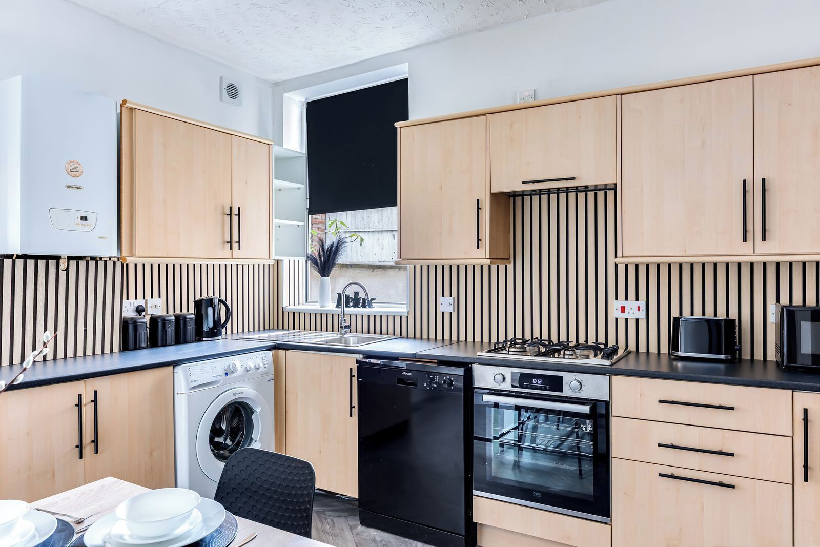 A compact kitchen with wooden cabinets, a built-in washing machine, a dishwasher, a stove, and a sink.