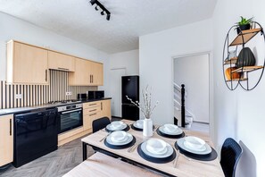 Eine moderne Küche mit Holzausstattung, einem schwarzen Kühlschrank und einem Esstisch für vier Personen.