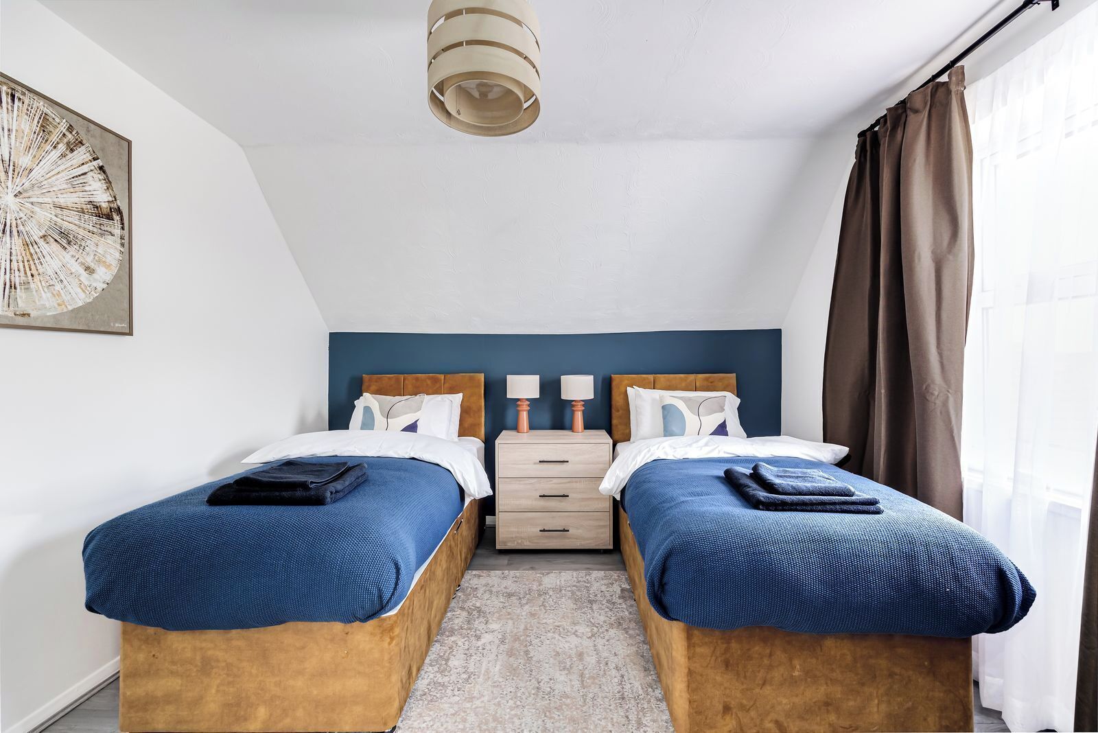 A hotel room with two beds, a nightstand, a lamp, and a ceiling light.