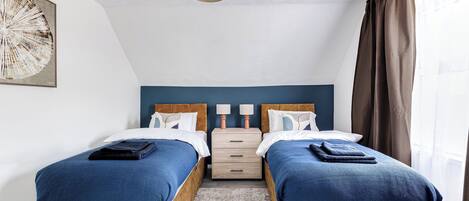 A hotel room with two beds, a nightstand, a lamp, and a ceiling light.