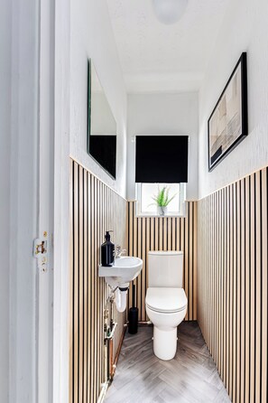 Ein schmales Badezimmer mit Toilette, Waschbecken und Fenster mit Pflanze.