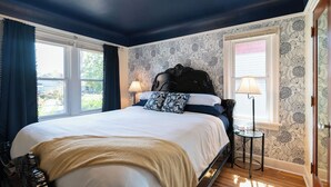 Een slaapkamer met een groot bed, twee bedlampen en een uitzicht op het buitenlandschap door twee ramen.