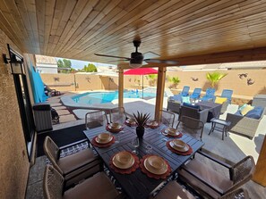 Une terrasse extérieure avec une piscine, une table à manger dressée avec des assiettes et des verres, et des chaises longues.