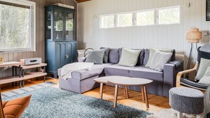 A cozy living room with a sectional sofa, a small round table, a blue cabinet, and a window with a view of trees.