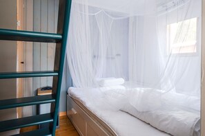 Ein Stockbett mit Baldachin, eine Holzleiter und ein kleiner Nachttisch mit einem Buch.