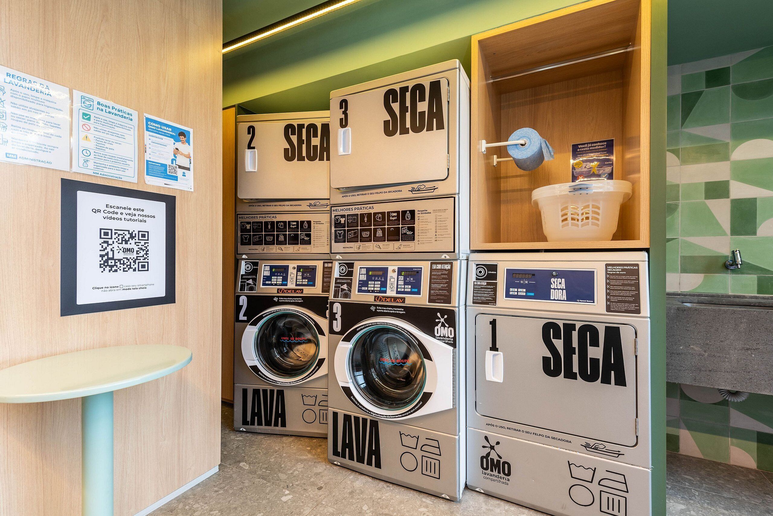 A laundry facility with multiple washing machines labeled 'SECA' and 'LAVA,' a QR code for tutorials, and a sink area.