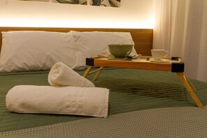 A neatly made bed with a green bedspread, a white towel, and a tray with a cup and a bowl. - Ape C AR piscina e academia prox Allianz (São Paulo)