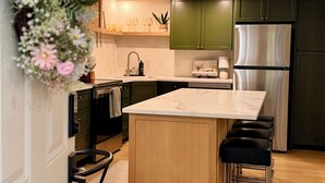 A modern kitchen with a central island, bar stools, a stainless steel refrigerator, and green cabinets. -  Comfort & Convenience Near Endless Local Amenities (Langley Township)
