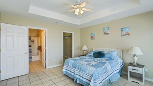 A bedroom with a bed, two bedside tables, a ceiling fan, and a door leading to a bathroom.