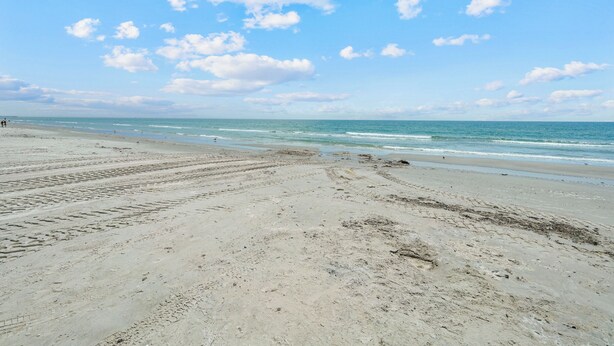 A beach with footprints leading to the water, a clear sky, and a calm sea.